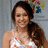 A woman with long brown hair in a ponytail wears a white halter top with red and blue patterns, standing against a light gray background with blurred colorful shapes.