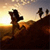 Silhouetted figures on a hill at sunset with a gradient sky transitioning from yellow to purple.