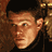 Pixelated static image of a person's face with dark hair and light skin tones, rendered in warm brown and orange hues against a darker background.