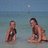 Two pixelated figures in swimwear stand on a beach with water and sky background; one figure faces forward, the other is turned slightly right.