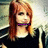 Pixelated static image of a person with long reddish-brown hair wearing a dark top and purple choker against a light background.