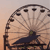 A pixelated Ferris wheel with dark passenger cars against a gradient sky background, featuring a dark blue structure with green accents at the base.