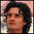 Pixelated close-up of a person with dark curly hair, light skin tone, and neutral expression against blurred background.