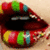 A pair of stylized lips with multicolored candy-like patterns on the lower lip, open mouth showing teeth and tongue.