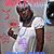 Pixelated image of a person in a white shirt with purple text, holding a dark object, against a gray background with pink and blue accents.