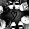 Black-and-white image of multiple sneakers with a heart symbol drawn on the ground between them.