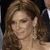 A pixelated close-up of a person with long brown hair, wearing a light-colored earring, against a dark background with a partial figure in the upper right.