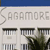 A pixelated building facade with 'SAGAMORE' text above three windows and a tree, under a blue sky strip.