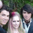 Group of four people with green foliage background, two individuals have dark hair and light-colored collared shirts, one has long blonde hair with pink streaks.