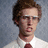 A pixelated image of a person with brown hair and glasses wearing a white shirt and red tie, next to a blue background with white text.