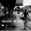 Black-and-white image of a woman in a flowing dress walking away on a sidewalk, with text overlay "dancer at heart" and a small heart symbol.