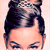 A close-up of a person's head with dark hair styled in an updo, wearing a small tiara with a patterned design.