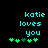 Pixelated cyan text 'katie loves you' above green heart symbols on black background, with animation changing one central heart from dark to light green.
