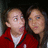 Two people in red jackets with white undershirts pose closely together, one person's head slightly turned left.
