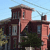 Pixelated static image of a multi-story building with brown and pink facades, windows, a chimney, and green foliage under a light blue sky.