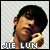 Pixelated image of a person with dark hair resting their chin on a hand, wearing a white shirt, with text 'DIE LUN' below, on a light gray diagonal striped background.
