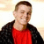 Pixelated image of a person wearing red shirt and black jacket against light background.