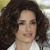 A pixelated close-up of a person with voluminous curly brown hair, light skin, and a white top against a blurred background.