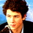 Pixelated close-up of a person with brown curly hair wearing dark clothing against a blue sky background.