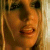 Pixelated static image of a person's face with warm orange and brown tones, showing partial facial features including eyes, nose, mouth, and hair against a light background.