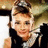 A static pixelated image shows a person with light brown hair styled in an updo, wearing dark clothing and holding a white object near their face.