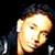 Pixelated static icon of a person's face with bright lighting and dark background, featuring visible pixelation artifacts and color blending in warm tones.