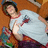 Pixelated image of a person in a white shirt with red trim lying on a brown surface, holding a colorful object.