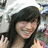 Pixelated static image of a person with long dark hair wearing a dark top, set against a blurred background with light and dark tones.