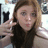 A pixelated portrait of a person with long brown hair and light-colored eyes, making a hand gesture near their face against a blurred background.