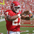 Pixelated image of a football player in red uniform holding a football, standing on a field with blurred background.
