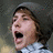 A pixelated image shows a person with brown hair and a gray beanie, mouth open in an expressive shout, next to light blue text on black background.