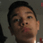 Pixelated close-up of a person's face with dark hair, light skin tone, and visible facial features against a muted gray background.