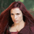 A pixelated close-up of a person with long reddish-brown hair against a blurred green background, wearing a dark top.