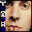 Pixelated close-up of a person's face with vertical text 'TRAVIS' on the left side, alternating blue and white block letters.