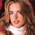 Pixelated close-up of a person with long brown hair wearing a white top against a dark background.