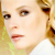 Pixelated close-up of a person's face with light skin, brown eyes, and blonde hair, wearing a white top with green accents.