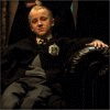 A person in dark robes sits on a chair with green text overlaying the image, changing across frames to form 'Draco Malfoy's Couch of Curue'.