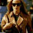 A pixelated image of a person with long blonde hair wearing sunglasses and a brown jacket, shown in four sequential poses with text reading "THERE SHE GOES JUST A WALKING DOWN THE STREET".