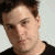 Static pixelated portrait of a person with short brown hair wearing a dark shirt against a light background.