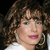 Pixelated close-up of a person with curly brown hair, light skin, and pink lips wearing a white top against a dark background.