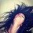 Pixelated image of a person with long dark hair against a light background, showing partial face and neck.