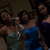 Group of people in a dimly lit setting with one person in blue clothing holding a microphone.