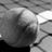 A grayscale pixelated image shows a partial view of a figure with a rounded head and dark hair, set against a light background with diagonal lines.