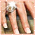 A hand holds a diamond ring with a large central stone and smaller side stones against a blurred background.
