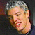 Pixelated close-up of a person's face with short light-colored hair, closed eyes, and a slight smile against a dark background.