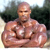 A pixelated image of a shirtless muscular man with a bald head standing outdoors with arms crossed.
