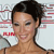 A pixelated close-up of a person with dark hair pulled back, wearing a strapless top, against a blurred background with red and white horizontal stripes.