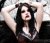 Pixelated image of a person with long dark hair wearing a white top, hands raised near head against light background.