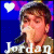 A 50x50 pixel animated buddy icon featuring a person with short brown hair wearing a gray beanie and dark jacket, displayed in two frames showing heart color change from white to pink against a blue background with purple accents.