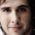 Pixelated close-up of a person's face showing eyes, nose, and mouth with light skin tone against dark background.